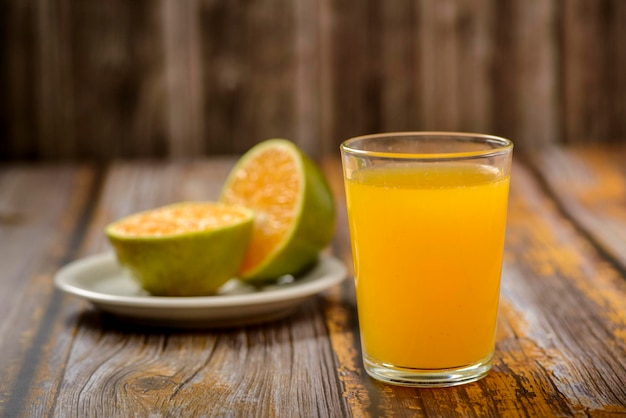 Orangensaft. Glas auf Holztisch mit einer in Scheiben geschnittenen Orange im Hintergrund.