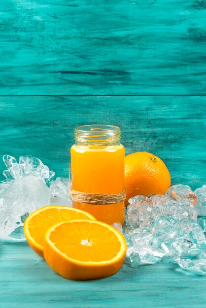 Orangensaft im Glas mit Orange auf Eis auf blauem Hintergrund, Kopierraum.