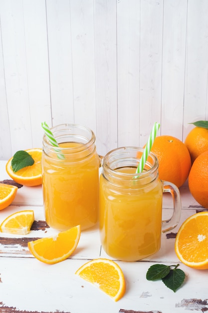 Orangensaft in den Glasgefäßen und in den frischen Orangen auf einem weißen hölzernen rustikalen Hintergrund.