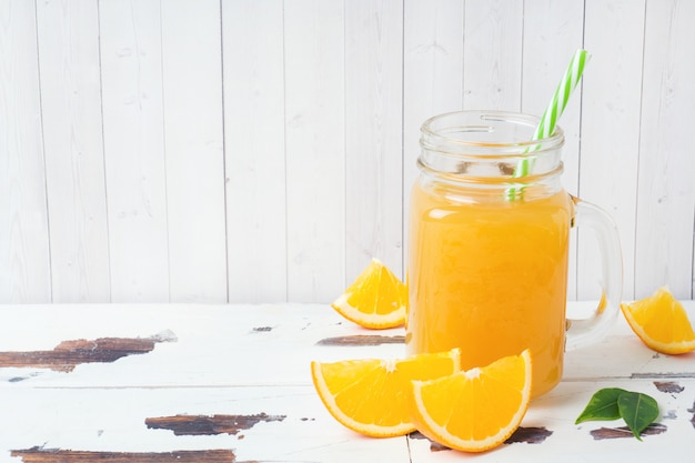 Orangensaft in den Glasgefäßen und in den frischen Orangen auf einem weißen hölzernen rustikalen Hintergrund.