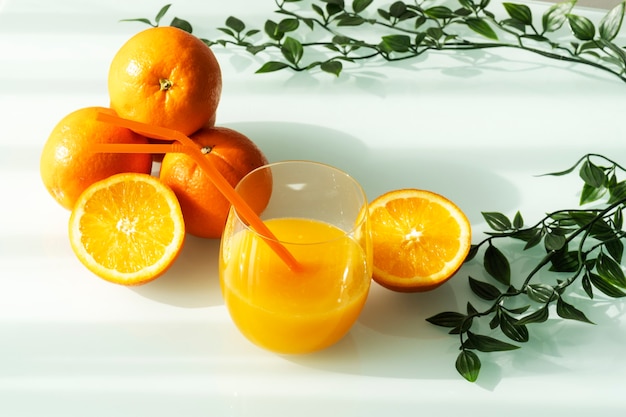 Orangensaft in einem Glas, umgeben von natürlichen Orangen und einigen grünen Blättern mit einem natürlichen hellen Sonnenhintergrund der Sonne