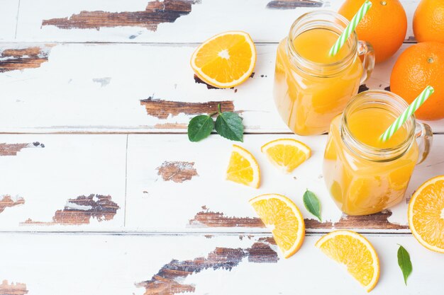 Orangensaft in glasgefäßen und frischen orangen auf einem weißen hölzernen rustikalen hintergrund.