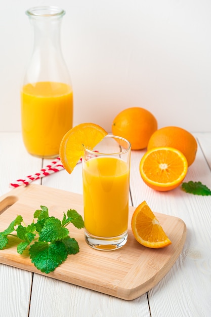 Orangensaft mit Glas und Minze erscheint nicht auf einem hellen Schreibtisch mit Dekanter. Seitenansicht, vertikal.