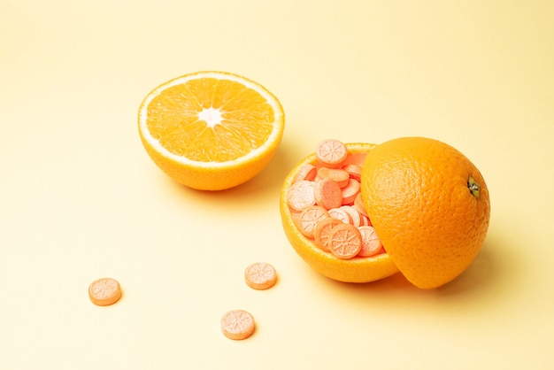 Orangenschale gefüllt mit Vitamin-C-Pillen und einer halben Orange auf einem Gelb