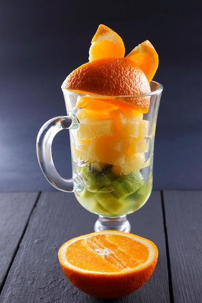 Orangenscheiben im Glas Fruchtcocktail auf schwarzem Hintergrund Orangenscheiben aus Ananas und Kiwi in einer Glasschüssel