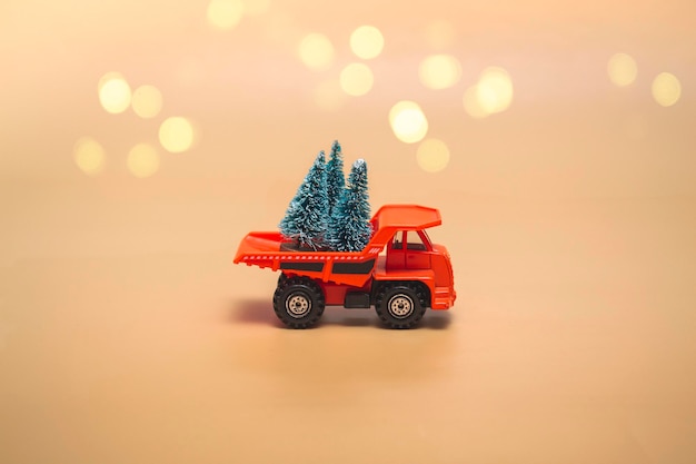 Oranger LKW mit Weihnachtsbäumen auf einem beigen Hintergrund mit Lichtern. Ferien-Konzept. Nahaufnahme, mit Kopienraum.