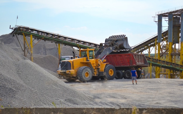 Oranger Traktor lädt Kies in das Auto auf der Baustelle in der Nähe des Trümmerhaufens