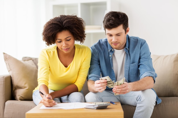 Foto orçamento familiar, finanças e conceito de pessoas - casal com papéis e calculadora contando dinheiro em casa