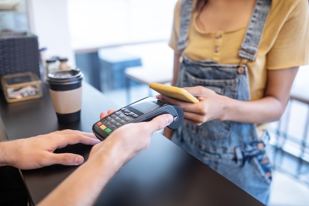 Foto orden de pago. manos delgadas femeninas que sostienen el teléfono inteligente amarillo cerca del cartel sobre el mostrador en el café