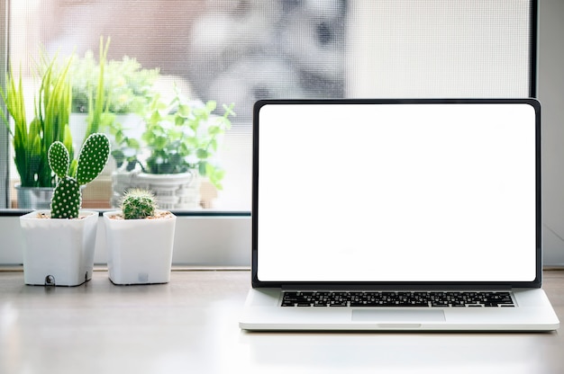 El ordenador portátil blanco de la pantalla en blanco con los cactus florece en la tabla de madera.