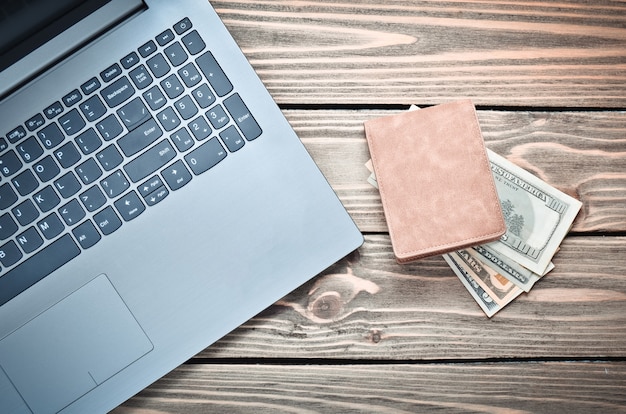 Foto ordenador portátil y un bolso con dinero en una mesa de madera. el concepto de trabajo en línea en internet, freelance. vista superior.