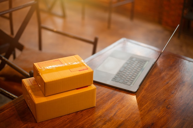 Foto ordenador portátil, caja de cartón, paquete de productos para entregar a los clientes.