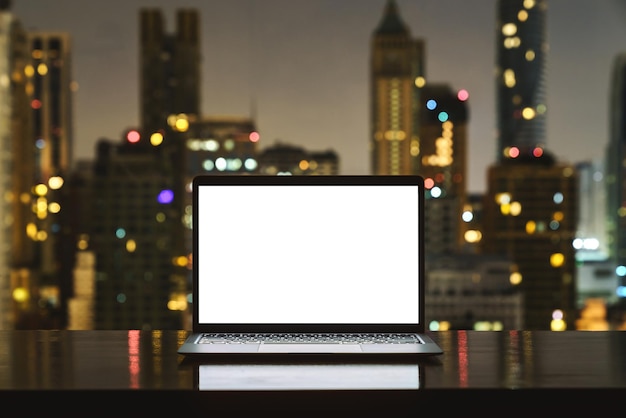 Ordenador portátil en el espacio de trabajo ciudad de pantalla en blanco en blanco sobre fondo de noche