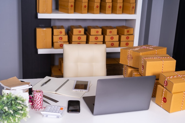 Ordenador portátil en la mesa y la caja de paquetes listo para su envío a los clientes en la oficina en casa