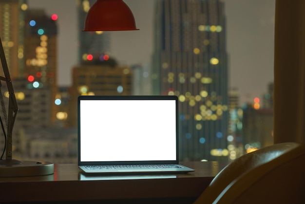 Ordenador portátil en la mesa con pantalla blanca ver a través de la ciudad sobre fondo nocturno