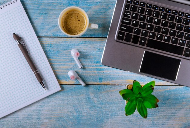 Ordenador portátil oficina cosas auriculares inalámbricos y taza de café bolígrafo vista superior tiro.