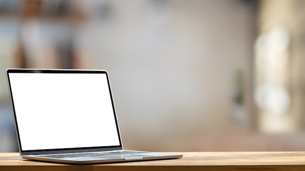 Ordenador portátil con pantalla en blanco blanco poniendo en la mesa de trabajo moderna con oficina cómoda borrosa como pantalla vacía para anunciar el concepto.