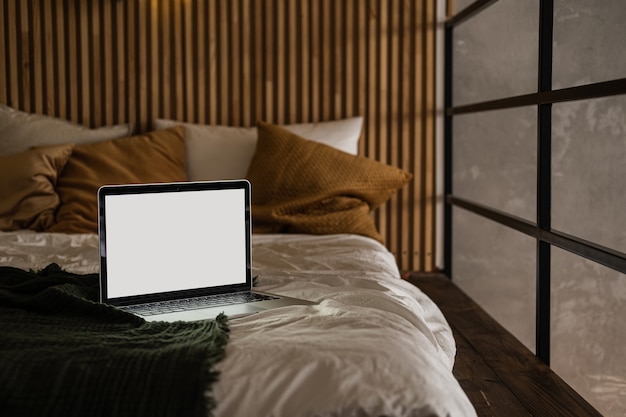 Ordenador portátil con pantalla en blanco en la cama con almohadas y ropa de cama.