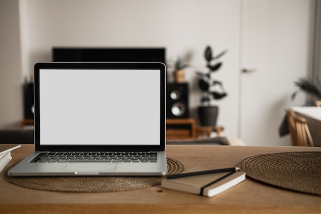 Ordenador portátil con pantalla en blanco, cuadernos de mesa de madera en la sala de luz solar cálida