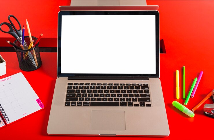 Foto un ordenador portátil con pantalla en blanco con papelería en mesa roja