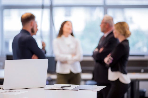 Foto ordenador portátil y portapapeles con la pluma en la mesa con empresarios defocused en el fondo