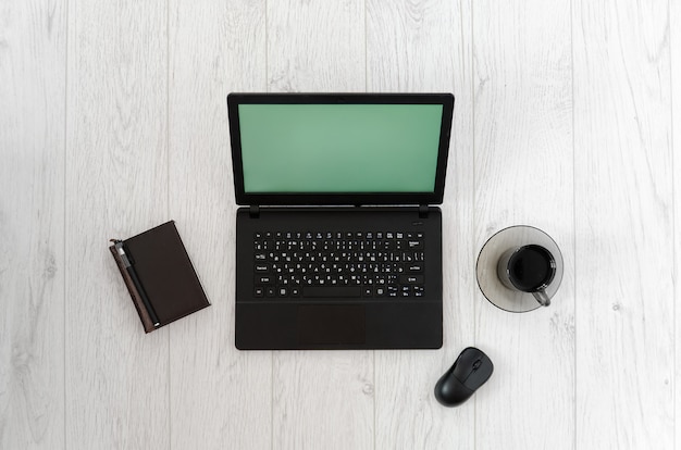 Ordenador portátil, ratón de la computadora, taza de café y cuaderno en una mesa de madera.