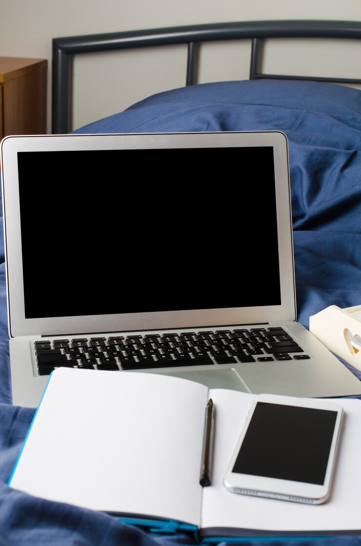 Foto ordenador portátil y teléfono inteligente, taza de café y cuaderno en la cama en el tiempo de la mañana. bosquejo.