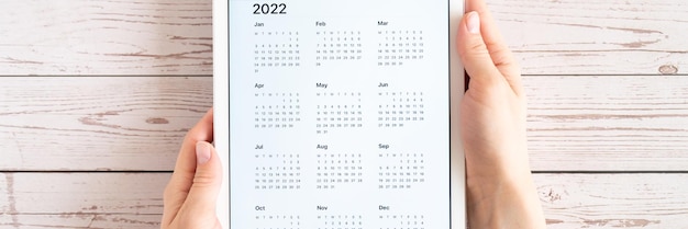 Ordenador tablet con una aplicación abierta del calendario para el año 2022 en una bandera de manos de mujeres