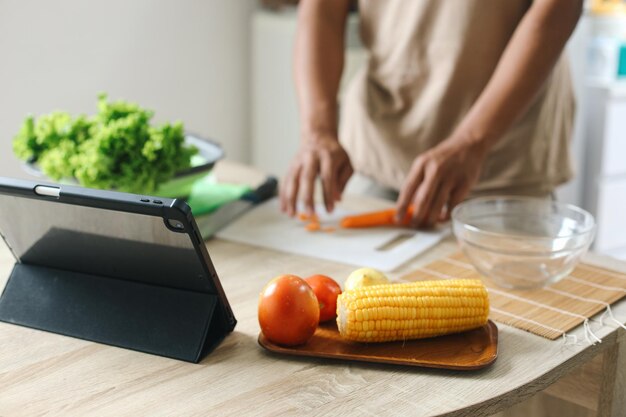 Un ordenador de tableta con maíz y tomate en una bandeja de madera con un hombre haciendo ensalada en el fondo