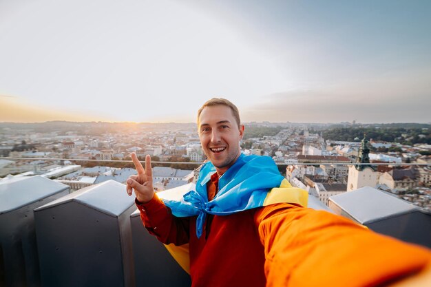 Ore pela UcrâniaxAA o homem fica com a bandeira nacional ucraniana e acenando rezando pela paz ao pôr do sol em LvivxAA símbolo da independência e força do povo ucraniano