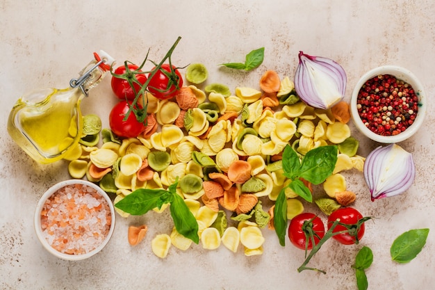 Orecchiette crudo con queso parmesano y tomates, albahaca, ajo y aceite en pared clara con pimienta en pared marrón claro. Ingredientes tradicionales para la preparación de pasta italiana. Vista superior.