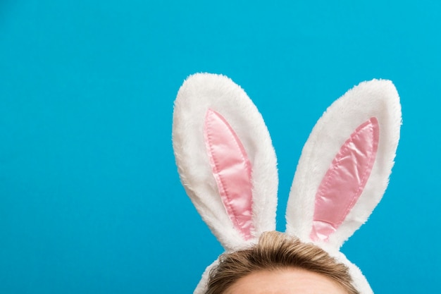 Orejas de conejo de Pascua Hembra con traje de orejas de conejo blanco contra un fondo azul brillante