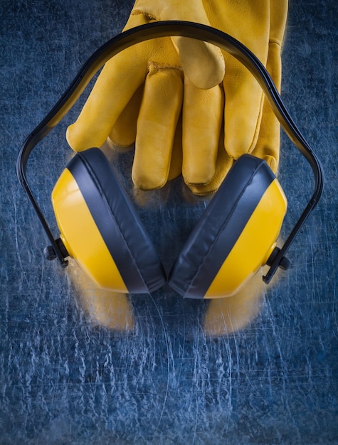 Foto orejeras con aislamiento acústico y un par de guantes protectores de cuero sobre el concepto de construcción de superficies metálicas rayadas