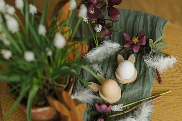 Orelhas de coelho elegantes de madeira e ovos naturais flores da primavera penas e ninho na mesa rústica close-up Feliz Páscoa Páscoa natureza morta Arranjo festivo e decoração na vista superior da fazenda