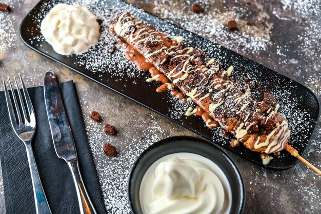 Oreos y Brownie Waffle Stick con cuchillo y tenedor de crema batida de chocolate servido en un plato aislado en un fondo oscuro vista superior café comida de postre