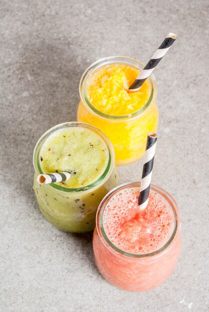 Organische Diätgetränke des Detox, selbst gemachte tropische Smoothies - Kiwi, Orange, Pampelmuse, in portionierten Gläsern, auf einer grauen Steintabelle. Copyspace Draufsicht