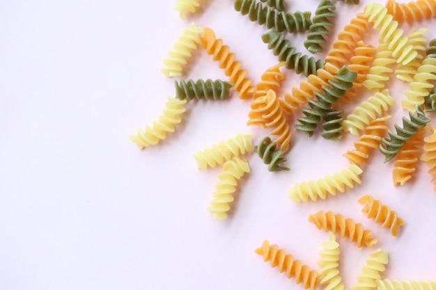 Organische Fusilli tricolore, die auf rosafarbenem Hintergrund verschüttet werden