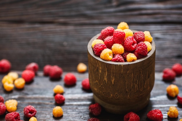 Organische gelbe und rote Himbeeren im Holztopf auf Holzhintergrund