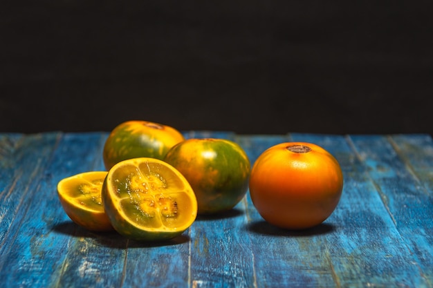 Organische Lulo- oder Naranjilla-Südamerika-exotische Frucht. Früchte auf alter blauer Tabelle und dunklem Hintergrund. Solanum quitoense, dunkles Futter