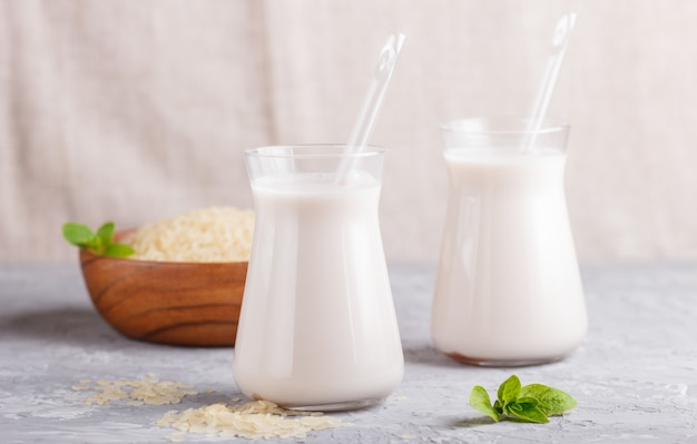 Organische nicht Milchreismilch in der Glas- und hölzernen Platte mit Reissamen auf einem grauen Beton.