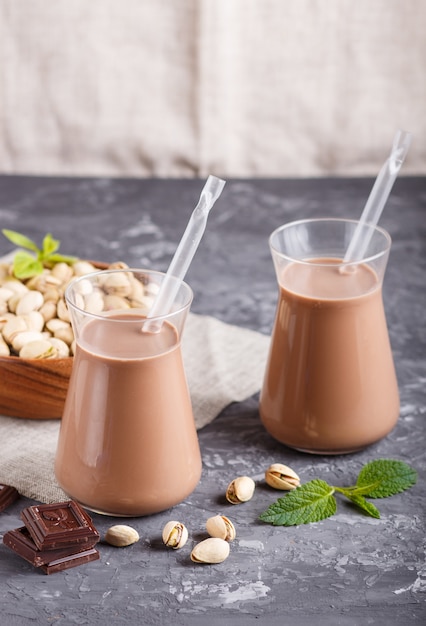 Organische nicht Molkerei Pistache-Schokoladenmilch in der Glas- und hölzernen Platte mit Pistazien auf einem grauen konkreten Hintergrund