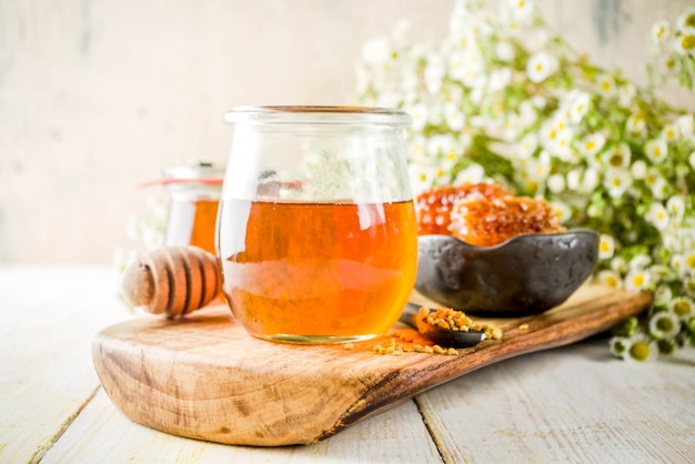 Organischer Blumenhonig, in den Gläsern, mit den Blütenstaub- und Honigkämmen, auf einem weißen Holztisch, mit Wildblumen