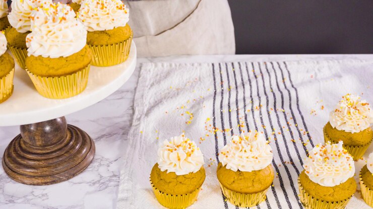 Foto organizando cupcake de especiarias de abóbora decorado com glacê de creme de manteiga italiano e granulado em um carrinho de bolo.