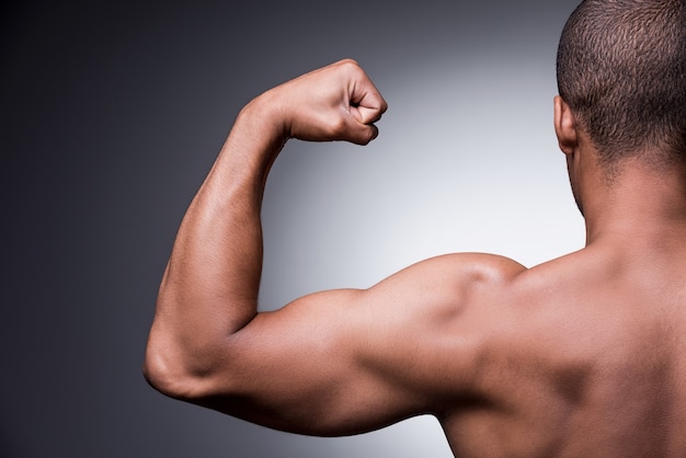 Foto orgulhoso de seu corpo perfeito. retrovisor de um jovem africano sem camisa, olhando para o bíceps