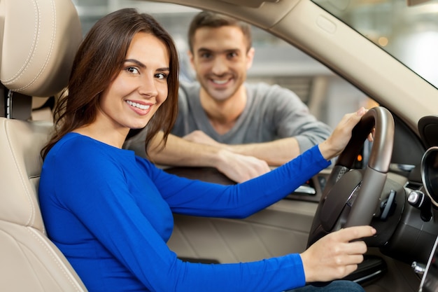 Orgulhoso de seu novo carro. lindo casal jovem está examinando um carro novo na concessionária