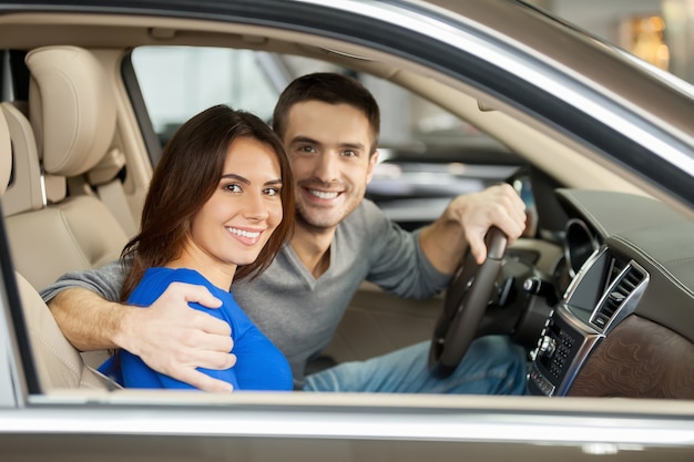 Orgulhoso de seu novo carro. Lindo casal jovem sentado no banco da frente do carro olhando para a câmera
