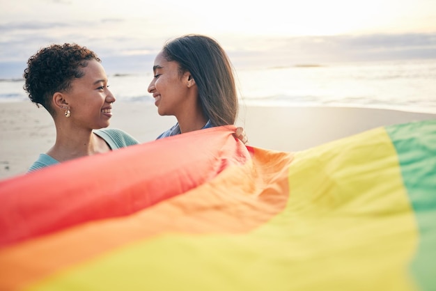 Orgullo bandera pareja lesbiana y libertad sonríen en la playa para romance feliz o cuidado en la naturaleza Arco iris amor y mujeres en el océano abrazan lgbt gay o fecha de orgullo de pareja o momento de relación romántica
