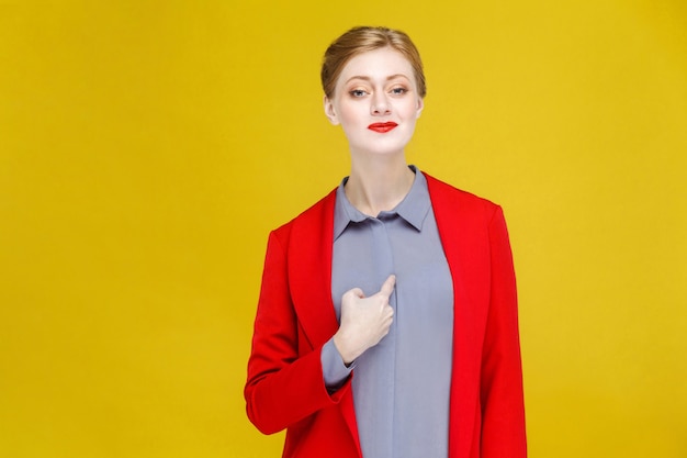 Orgullosa mujer de negocios de cabeza roja jengibre en traje rojo apuntando a sí mismo