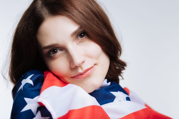 Orgulloso estadounidense. Hermosa joven de cabello castaño apoyando su mejilla en la bandera estadounidense, envuelta en ella
