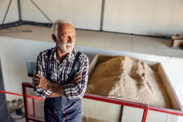 Un orgulloso trabajador de la fábrica senior está de pie con los brazos cruzados y apoyado en la barandilla